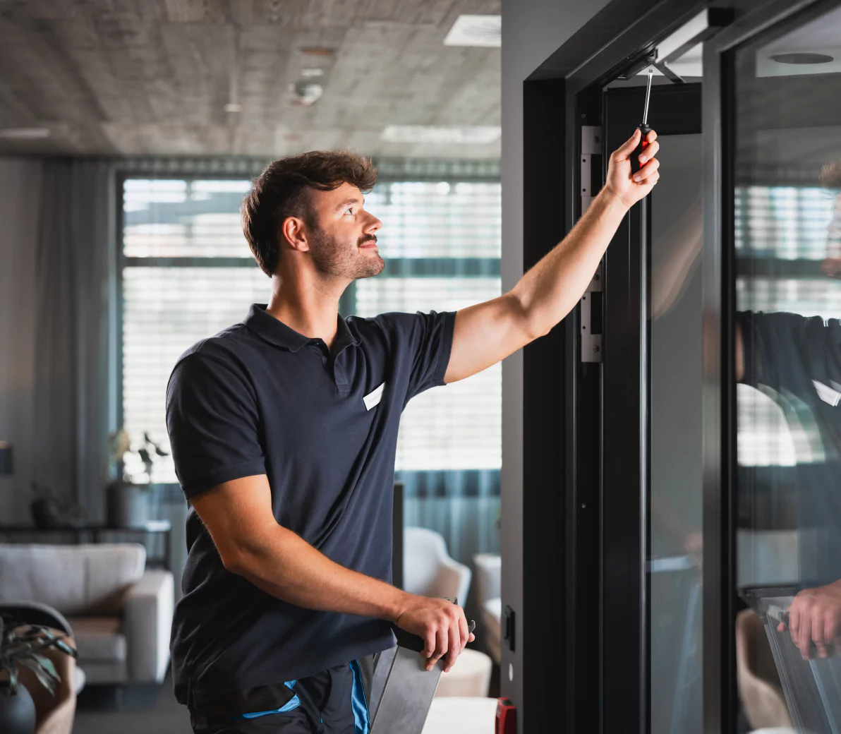 Maintenance technician in a navy polo shirt using a screwdriver to adjust a door mechanism.